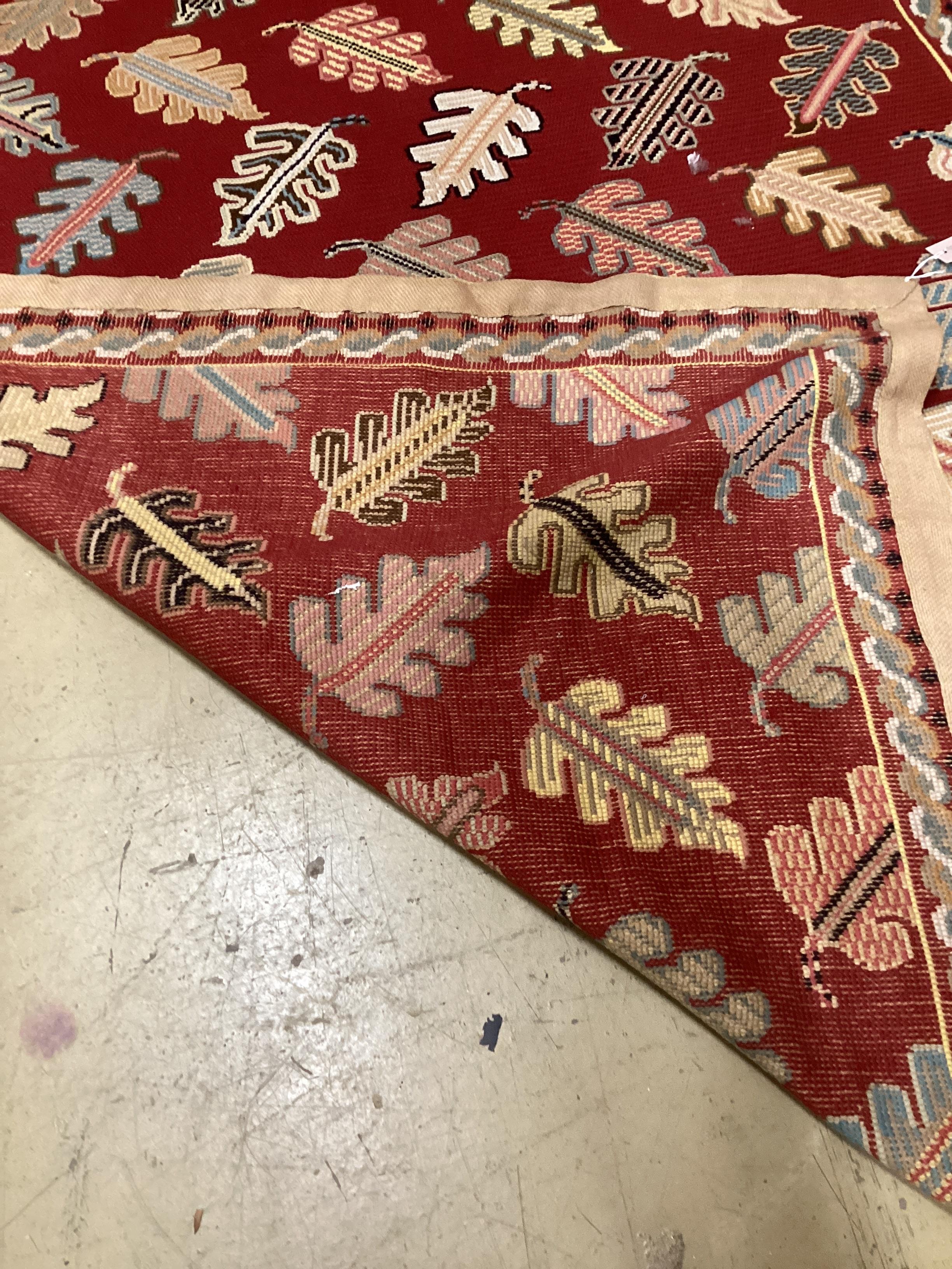 A Portuguese polychrome red ground rug woven with stylised leaves 236cm x 170cm.